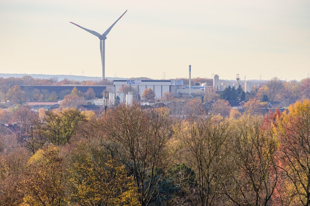 wind-turbine-above-autumn-trees-and-industrial-buildings-rmxmm9sabpe